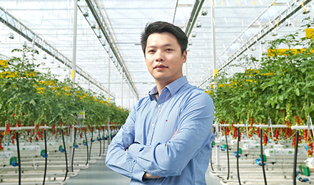 Dan Xu in front of crops in a greenhouse